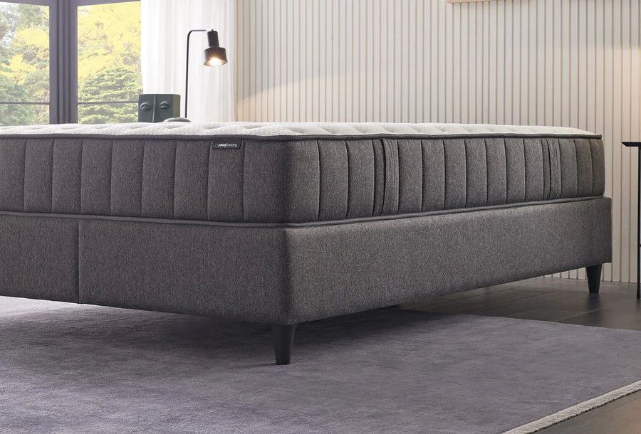 Zijaanzicht van het Ionic Energy matras op een grijze bedbodem in een slaapkamer met lamp