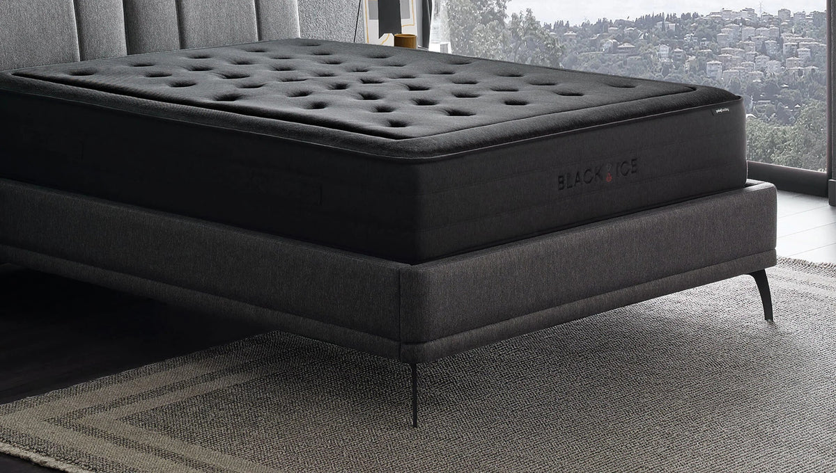 Black Ice matras op een grijs bed voor een raam met uitzicht op de stad