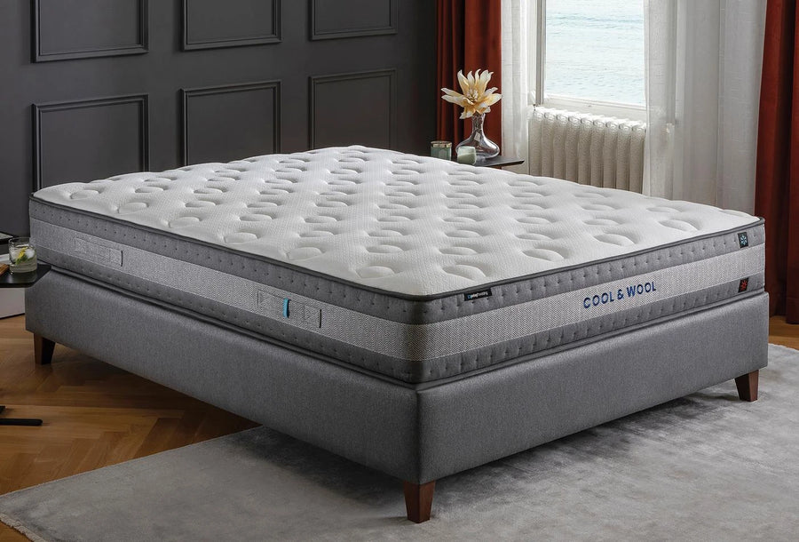 Cool & Wool matras met naam op de zijkant op een grijs bed bij het raam