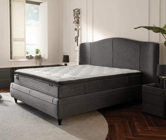 Orthopedic Support matras op een grijs gestoffeerd bed met gebogen hoofdbord