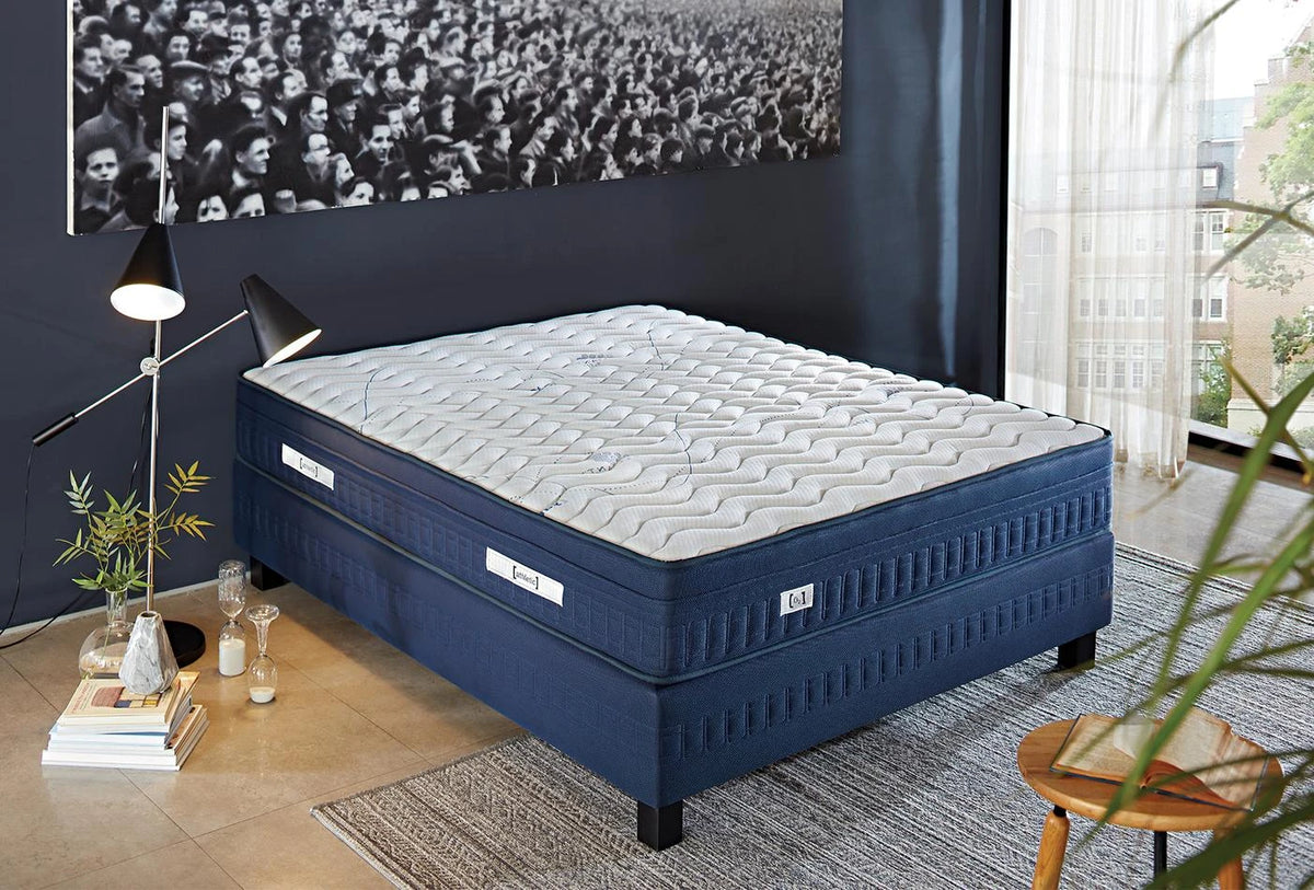 Athletic matras met donkerblauwe zijkant op een blauwe boxspring in een slaapkamer met fotowand