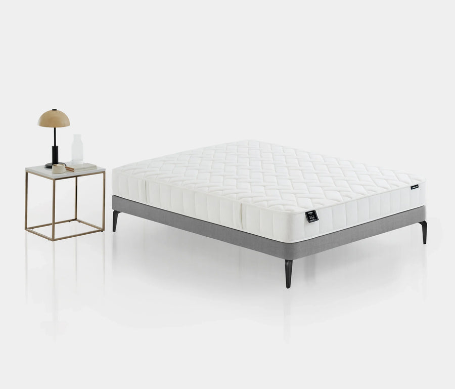 Supreme Star matras op een grijs bed naast een nachtkastje met lamp