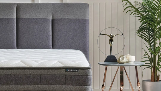 Dream Line matras op een grijze boxspring voor een gestoffeerd hoofdbord, naast een bijzettafel