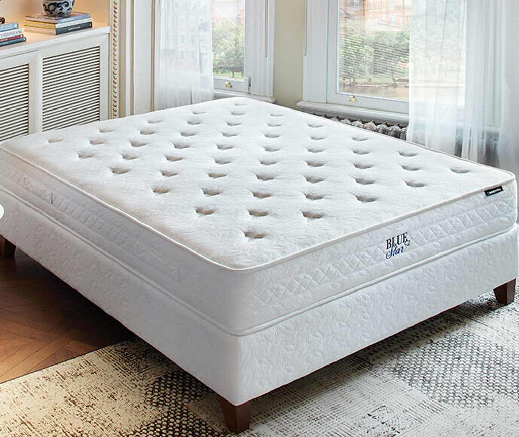 Blue Star matras met gecapitonneerd wit oppervlak op een wit bed in een lichte slaapkamer